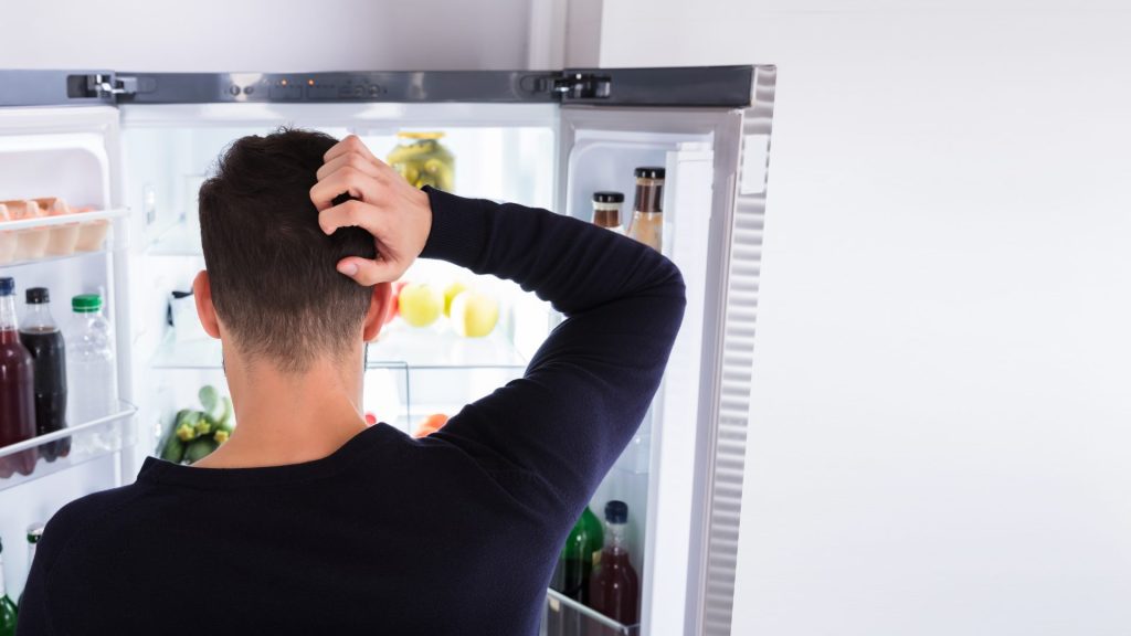 Férfi hűtőhiba miatt vakarja a fejét egy nyitott hűtő előtt – HűtőŐr segíthet megelőzni az ilyen helyzeteket.