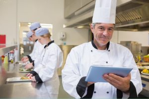 Férfi szakács önellenőrzést végez egy konyhában: hőmérsékletet mér és adatokat rögzít egy digitális eszközön.